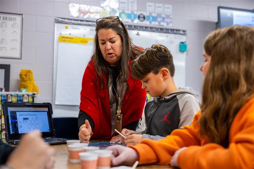  Teacher leaning down talking to two students.
